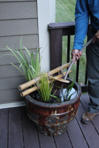 man filling up a pot with plants in it and a bamboo fountain on top…